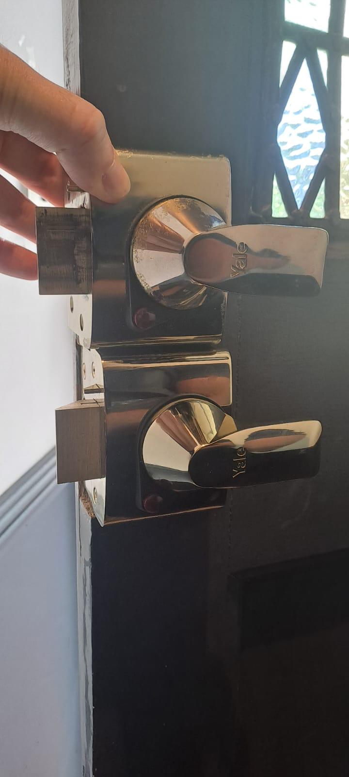 Close-up view of two Yale deadbolt locks installed vertically on a wooden door, with shiny chrome finish and thumbturn handles.